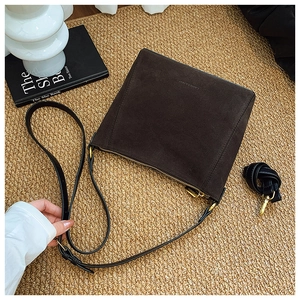 Detail of dark brown suede bucket bag with gold zipper on beige woven carpet backdrop