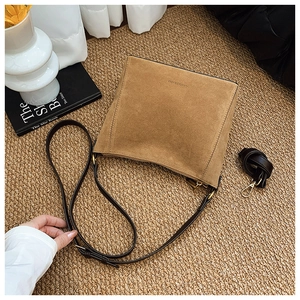 Flat lay of caramel suede bucket bag with leather straps on a woven mat with flowers