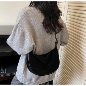 Detail of a black suede half-moon crossbody bag styled with a grey knitted sweater