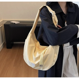 Detail of light yellow textured dumpling bag with 'R' patch and spacious design