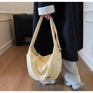 Detail of cream-colored large canvas crossbody bag with white A-letter patch and side tassels