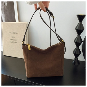 Macro shot of dark brown suede shoulder bag with gold zipper and embossed logo details