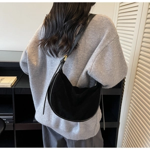 Black crescent shoulder bag in matte suede fabric worn by a model in a minimal setting