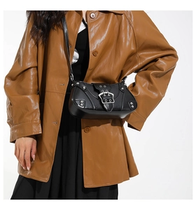 Detail of black glossy PU leather underarm bag with silver buckle on a brown trench coat