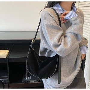 Detail of a black suede crescent moon bag with thin leather strap on a model's shoulder