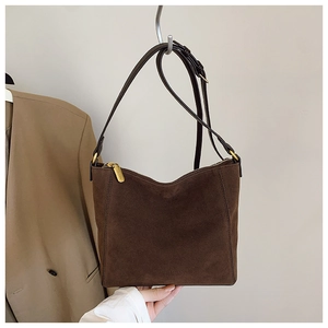 Detail of dark brown suede bucket bag featuring golden hardware and leather strap