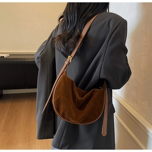 Brown suede half-moon bag worn on shoulder with grey suit in a stylish interior