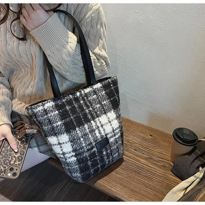 Close-up of black and white plaid plush tote bag with slim black handles and soft texture