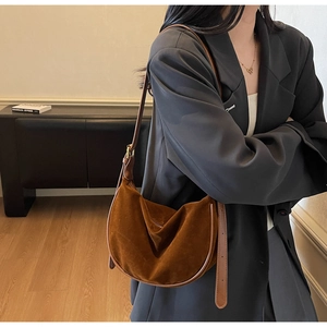 Brown suede crescent bag shown with adjustable shoulder strap worn by model in black suit