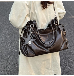 Détail du grand sac cabas en cuir marron avec breloque étoile porté sur un trench clair
