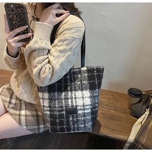 Detail of black and white plaid plush tote bag with leather strap and logo patch