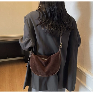 Detail of dark brown suede crescent bag with silver zipper and slim strap on grey blazer