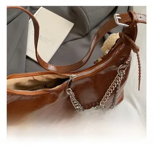 Close-up of brown crescent underarm bag with glossy oil-wax texture and silver metal chain