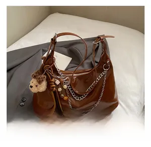 Detailed close-up of brown patent leather tote with silver chain and cute charms on bed