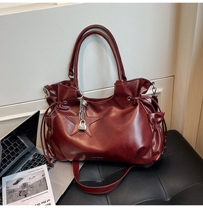 Detail der weinroten Shopper-Tasche mit Sternanhänger und Metallschloss auf Ledersitz