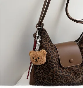 Detail of leopard print tote with brown leather strap and plush bear charm accent