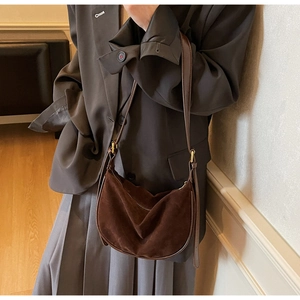 Detail of a dark brown suede dumpling bag with slim strap shown on a model