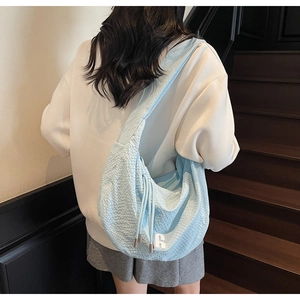 Detail of light blue textured fabric shoulder bag with thick drawstring and number 6 patch