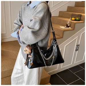 Detail of black glossy faux leather hobo bag with silver chain and bear charm detail