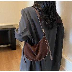 Detail of dark brown suede hobo bag with leather strap and gold buckle worn on shoulder