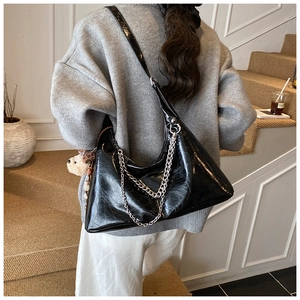 Detail of a black glossy shoulder bag with chunky silver chains and a plush bear charm