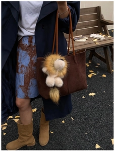 Braune Wildleder-Tote Bag mit Plüschlöwen-Anhänger in warmer herbstlicher Außenumgebung
