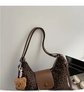 Detail of leopard print hobo bag featuring brown leather flap and cute plush bear charm