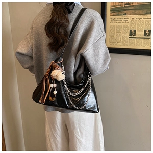 Back view of a black glossy leather half-moon shoulder bag with silver chain and bear charm