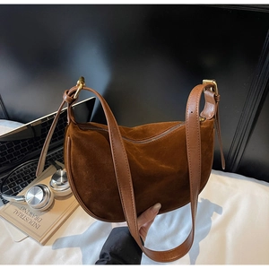 Close-up of brown suede moon bag with gold hardware and leather strap in office setting