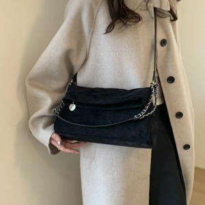 Detail of black quilted suede shoulder bag with silver chain and metal charm on wool coat