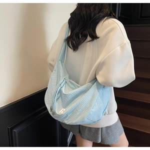 Detail of light blue dumpling bag showing woven texture and white R logo on shoulder strap