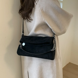 Detail view of a black quilted suede shoulder bag with silver chain strap on a model coat