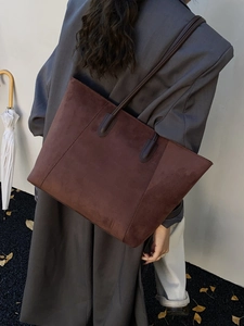 Brown suede tote bag worn by a model in an outdoor autumn setting with leaves
