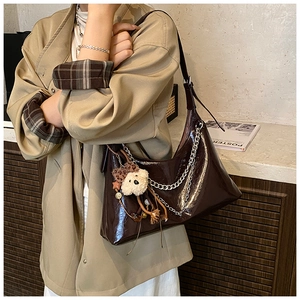 Detail of dark brown glossy shoulder bag with silver chain and plush bear charm