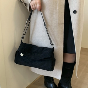 Detail of black quilted suede shoulder bag with silver chain strap and matte texture finish
