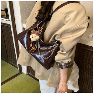 Detail of dark brown patent leather crescent bag with silver chain and plush charm