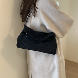 Detail of black suede-textured crossbody bag with silver chain strap worn by a model