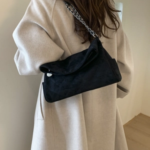 Detail of black quilted suede shoulder bag with silver chain strap on light coat