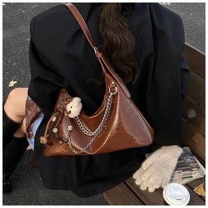 Brown glossy shoulder bag with silver chain and cute bear charm in autumn outdoor setting
