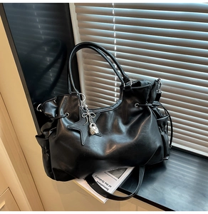 Detail der schwarzen Shopper-Tasche mit Kordelzug-Falten und einem Stern-Anhänger aus Metall