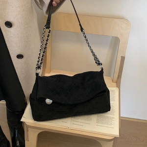 Detail of black quilted suede shoulder bag with silver chain and metal buckle on chair
