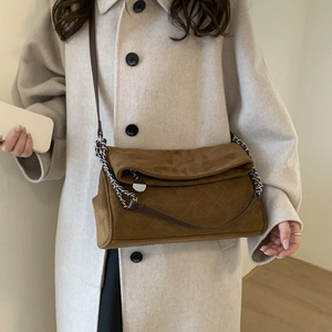 Detail of brown suede crossbody bag featuring diamond quilting and metal chain strap