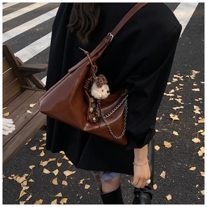 Detail of caramel leather shoulder bag with silver chain and cute plush dog charm