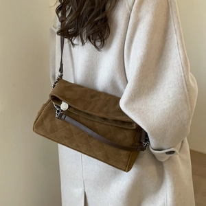 Close-up of brown suede quilted shoulder bag with chain strap on beige winter coat