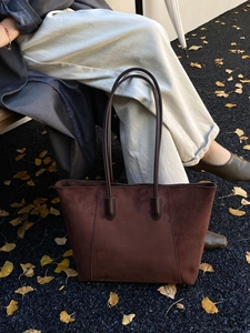 Detail of dark brown suede tote bag with long leather handles in an autumn outdoor setting