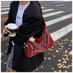 Detail of dark red glossy leather shoulder bag with a thick metal chain and plush charm