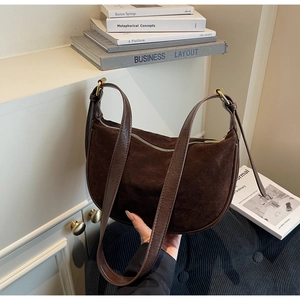 Detail of dark brown suede hobo bag with gold hardware held in a stylish indoor setting