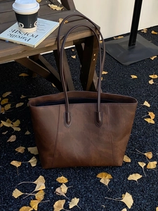 Detailed close-up of dark brown tote bag with vintage texture on fallen autumn leaves