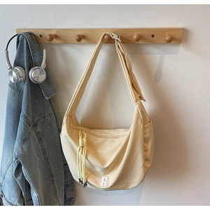 Detail of light yellow crescent crossbody bag with textured fabric and R label on wood hook