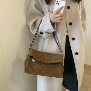 Detail of brown suede crossbody bag featuring quilted patterns and a silver chain strap